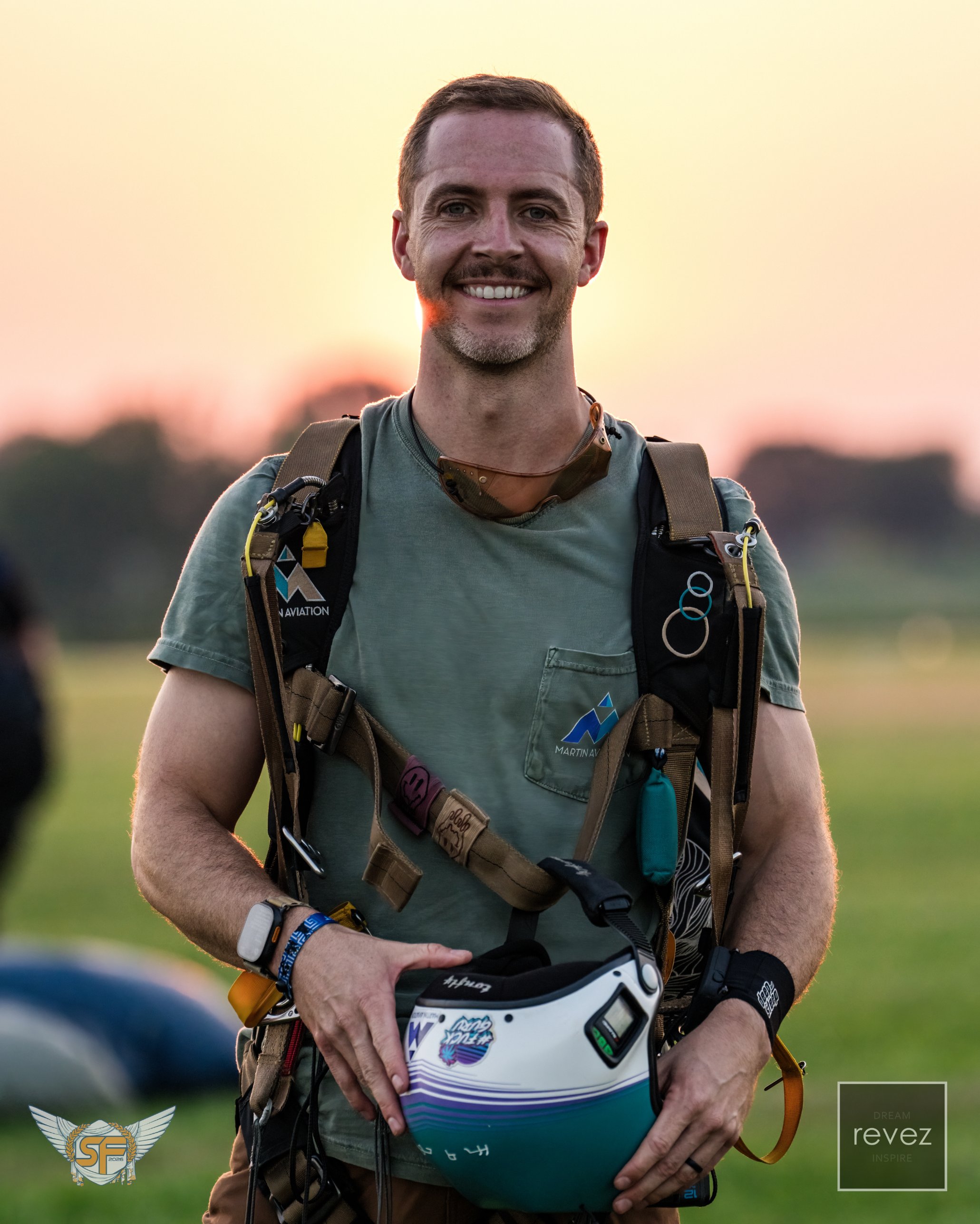 David Ball at a drop zone at sunset, skydiving rig on, holding his helmet